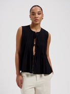 Black sleeveless pleated blouse with front tie closure and flowy fit by Nous Sommes Labels 