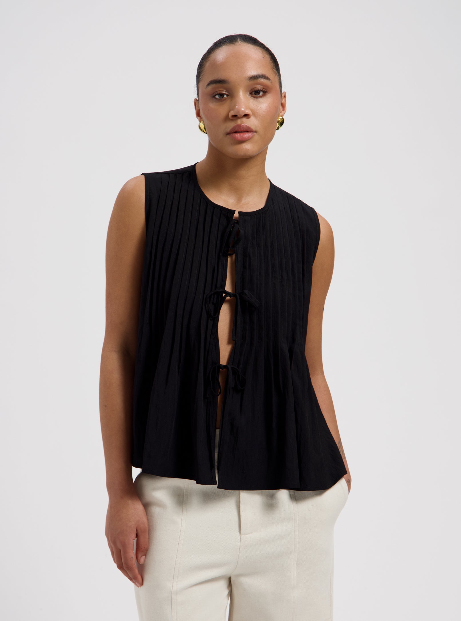 Black sleeveless pleated blouse with front tie closure and flowy fit by Nous Sommes Labels 